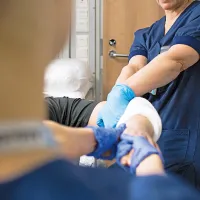 Kaksi hoitajaa laittaa potilaalle kipsiä. 